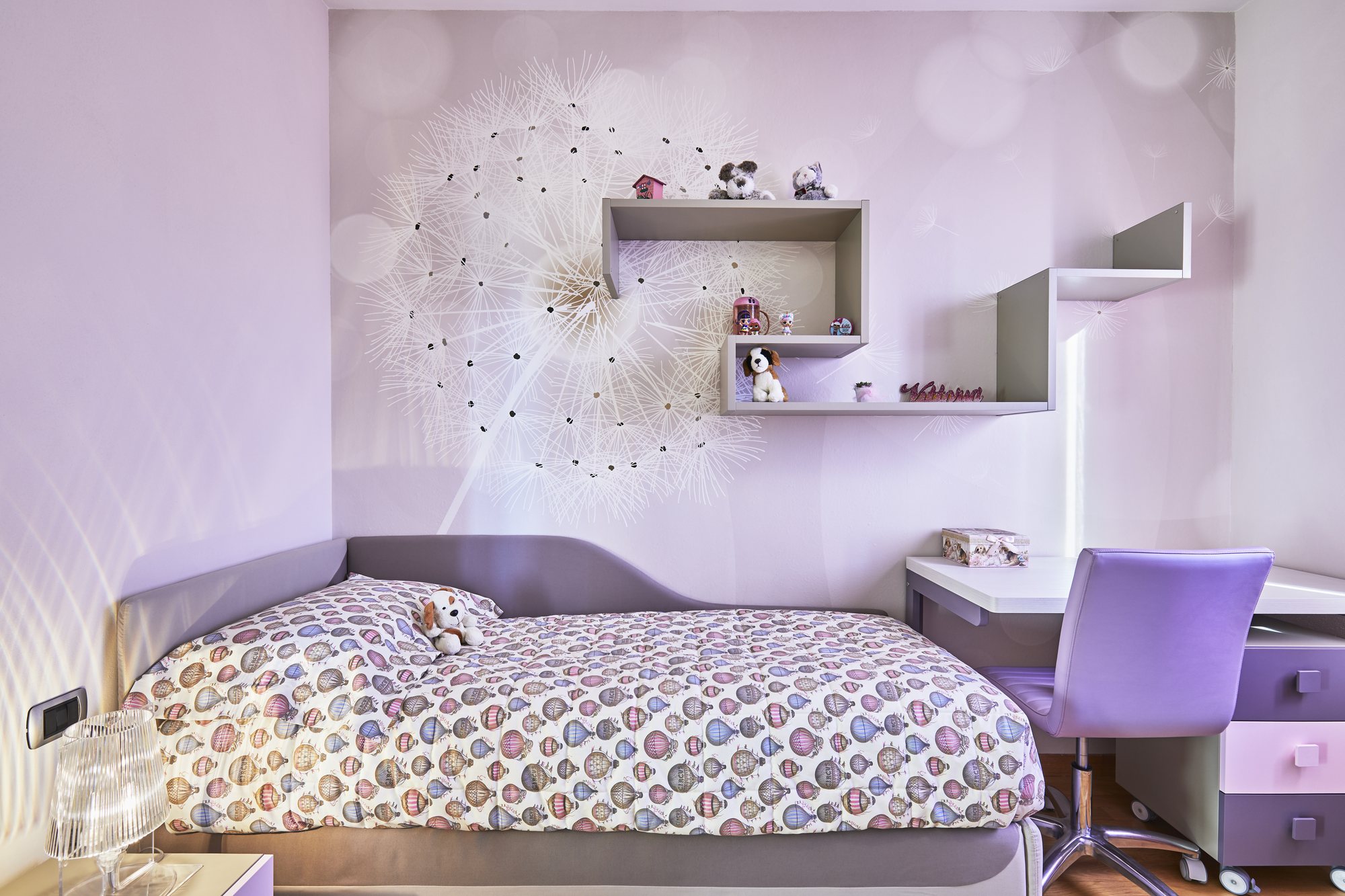Cameretta lilla con murale a soffione, letto imbottito, scrivania integrata e sedia viola: coordinata fin nei dettagli.