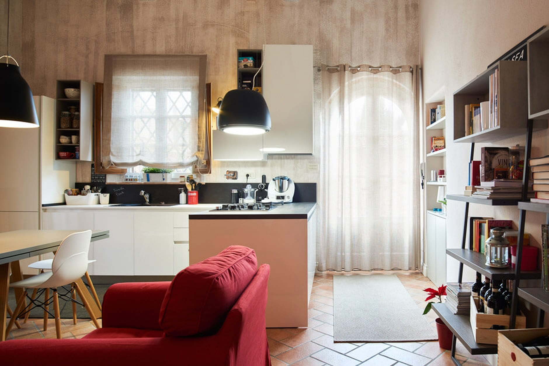 Cucina bianca e nera aperta sul soggiorno, con divano rosso e pavimento in cotto originale.