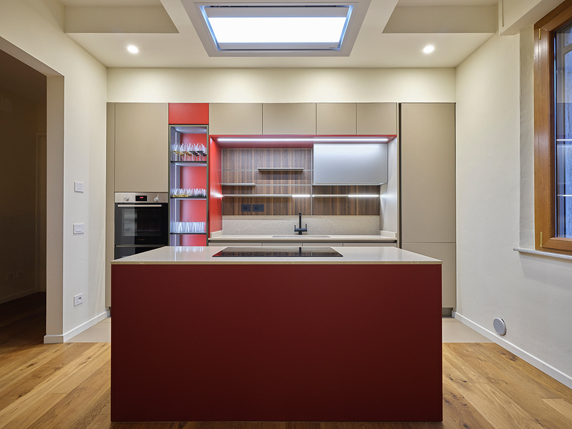 Cucina con isola laccata bordeaux, colonne chiare e faretto a soffitto.