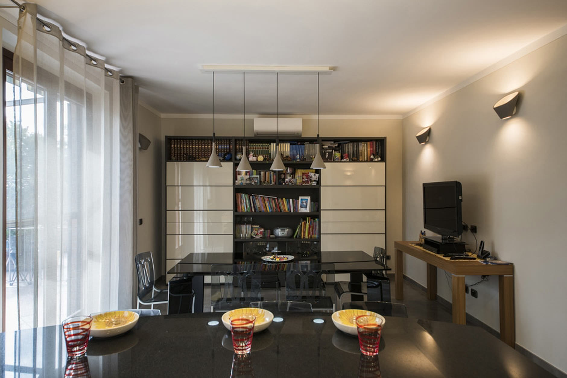 Zona pranzo con tavolo nero lucido, madia a due toni e lampadario di design.