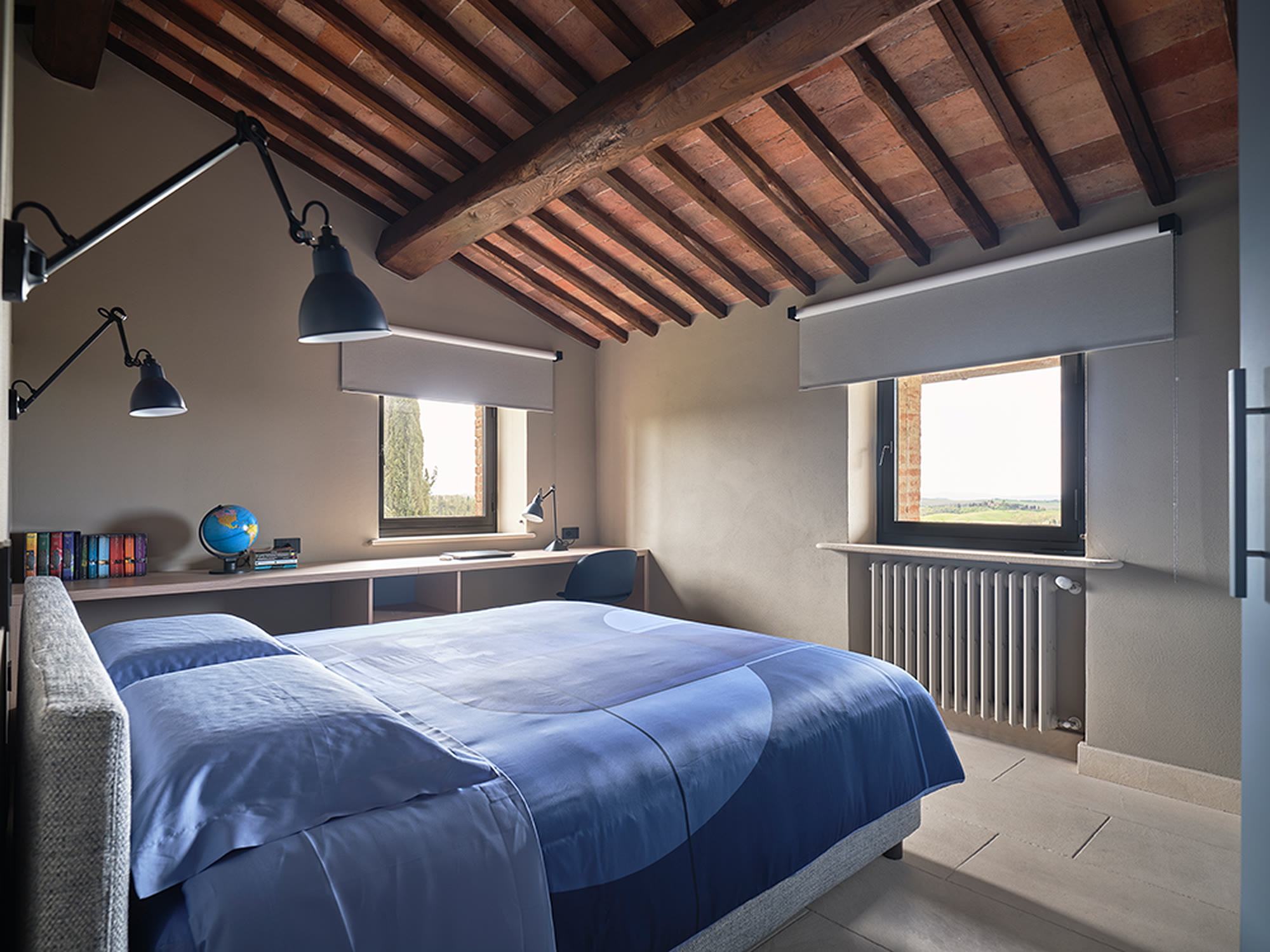 Camera mansardata con letto blu, travi a vista e lampade a parete orientabili.