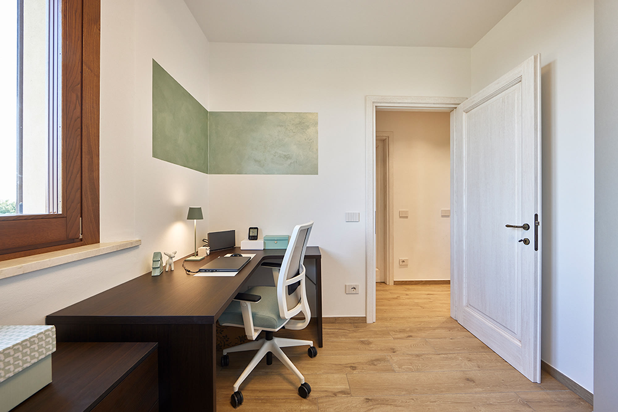 Studio con scrivania scura su misura, sedia ergonomica e parete verde salvia.