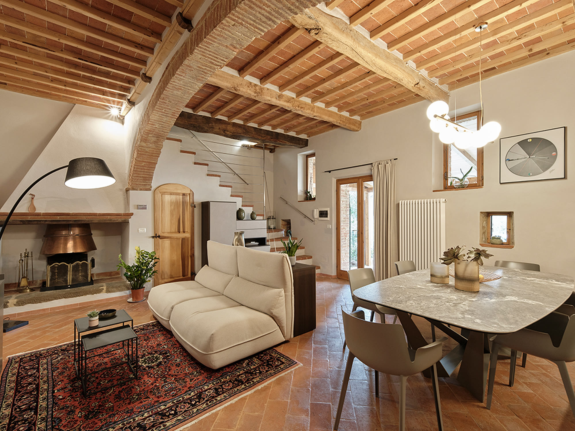 Living di casale con camino in pietra, divano bianco e tavolo in ceramica.