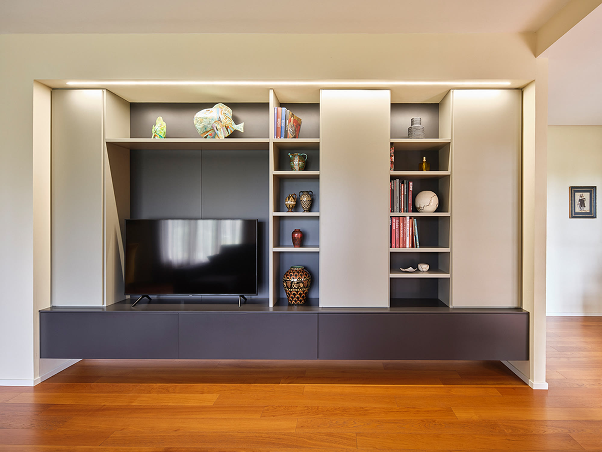 Parete attrezzata legno e grigio con TV e vani a giorno illuminati.