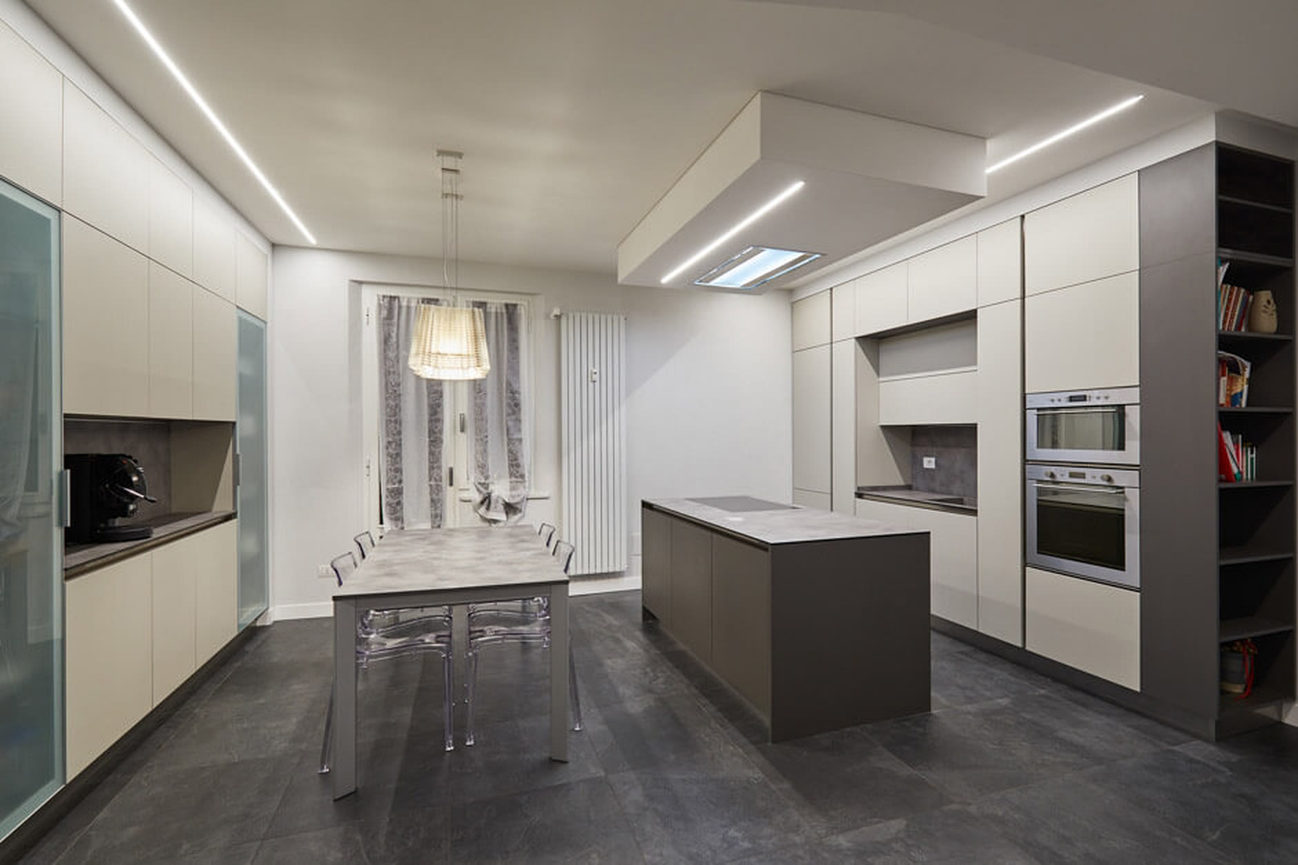 Cucina grigio chiaro con isola scura e luci lineari nel controsoffitto.