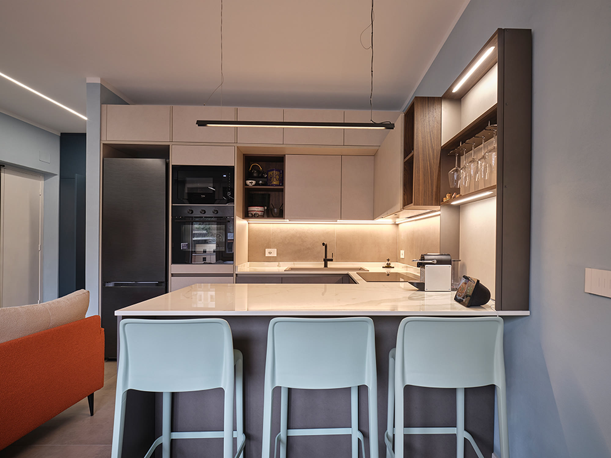 Cucina chiara con penisola in legno chiaro e sgabelli neri, aperta sul living.