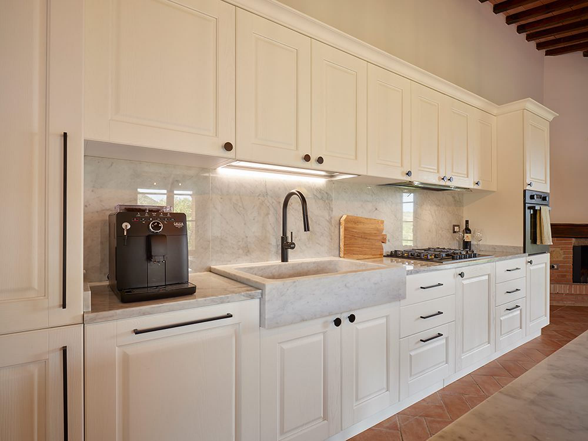 Cucina classica bianca con lavello in ceramica e pavimento in cotto.