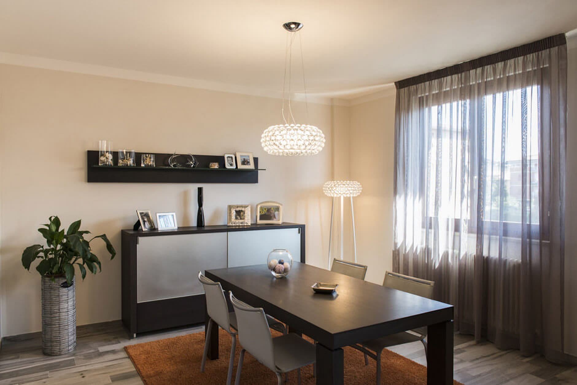 Zona pranzo con tavolo scuro, mensola a parete e lampadario a sfera.