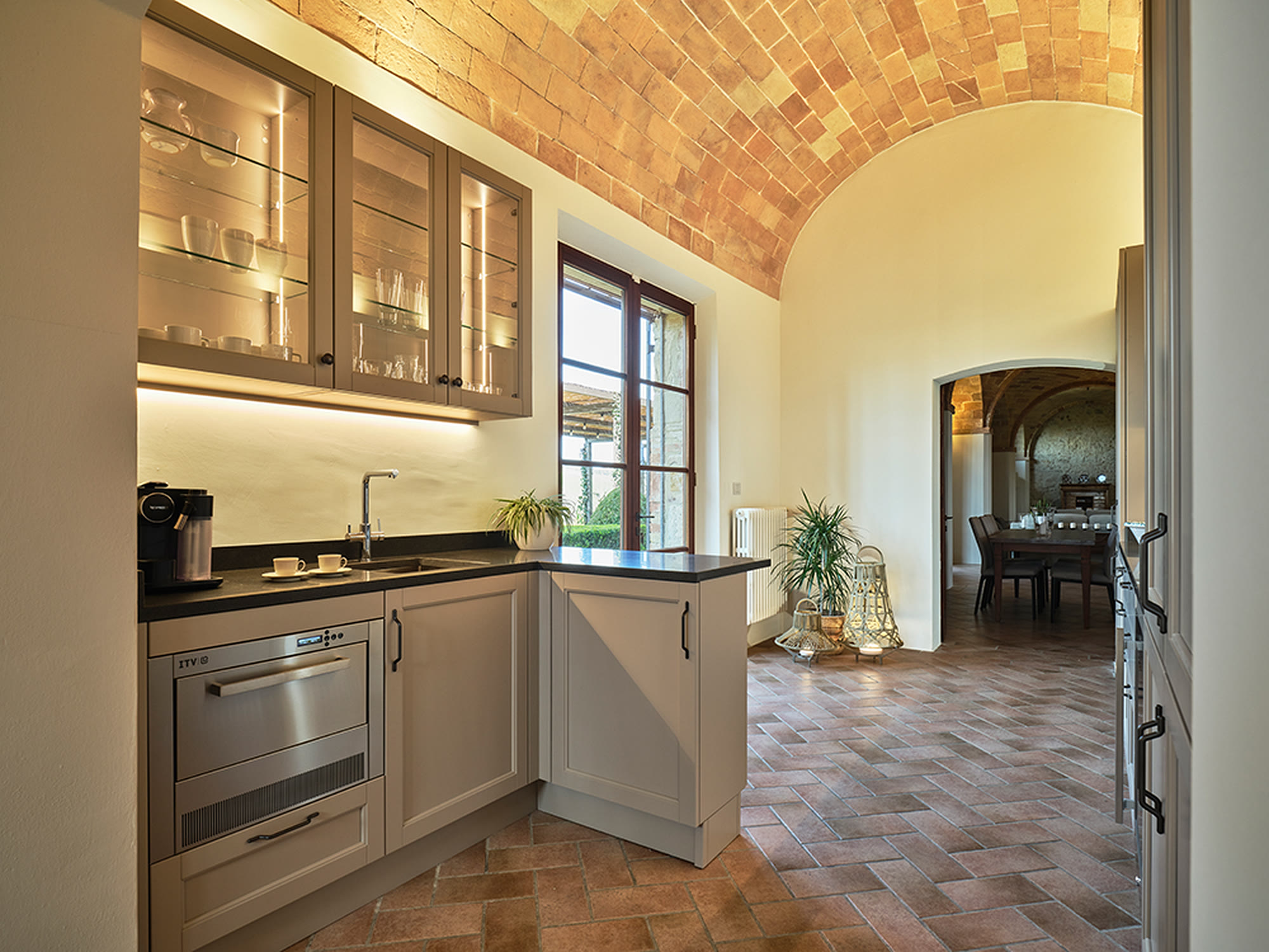 Cucina classica sotto volte in cotto con vetrinette illuminate e piano scuro.