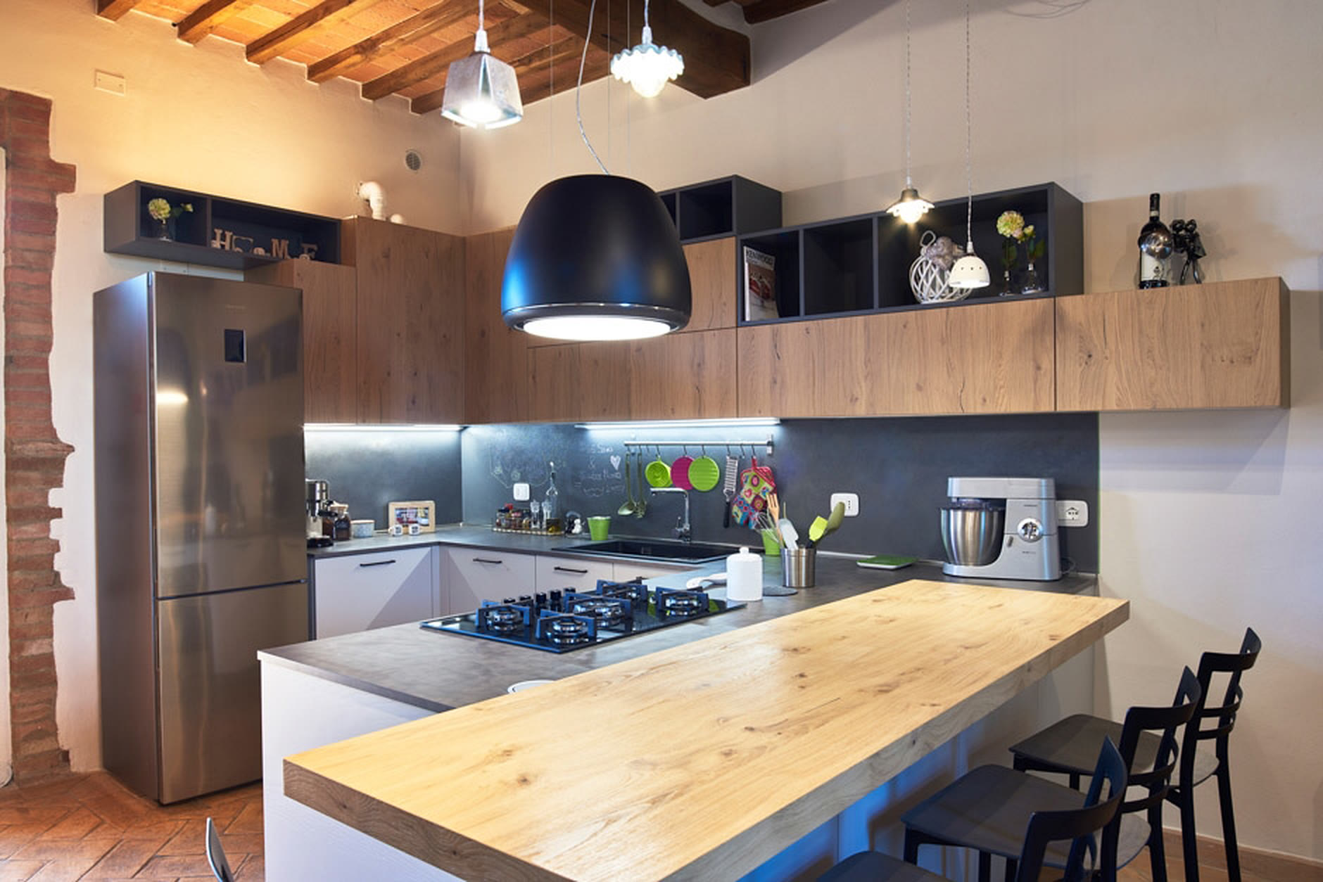 Cucina con cappa nera, isola in legno e frigorifero side-by-side in acciaio.