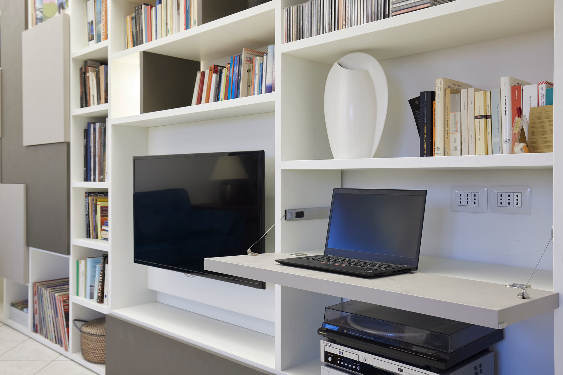 Parete attrezzata bianca con postazione di lavoro integrata tra le librerie.