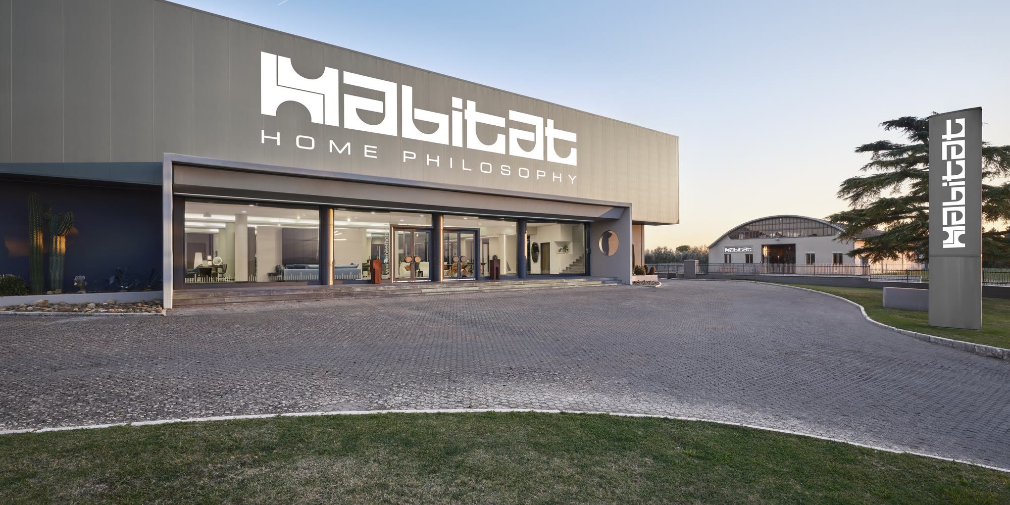 Showroom Habitat Arredamenti ad Asciano (Siena): la facciata con il logo Habitat Home Philosophy al tramonto, 2500 m² di arredamento in esposizione